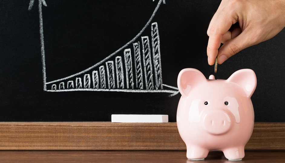 Close-up Of A Hand Putting A Coin Into Piggy Bank