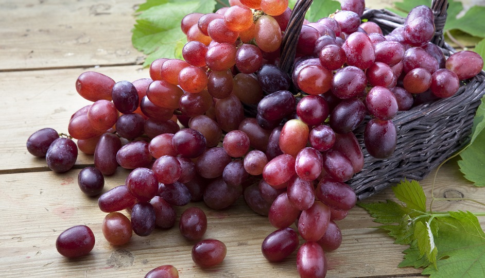 Red grapes in braided basket on wooden table